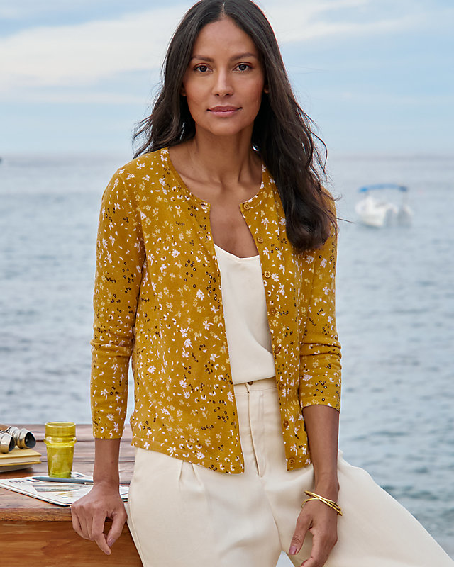 A woman in a gold floral merino cardigan sweater. Shop women's sweaters.