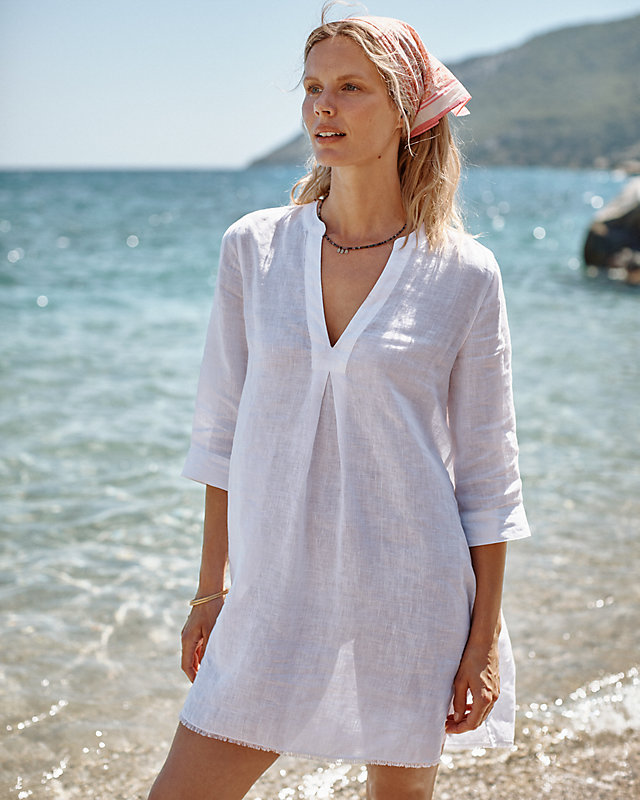 A woman in a white relaxed-linen beach dress. Shop women's swimwear.